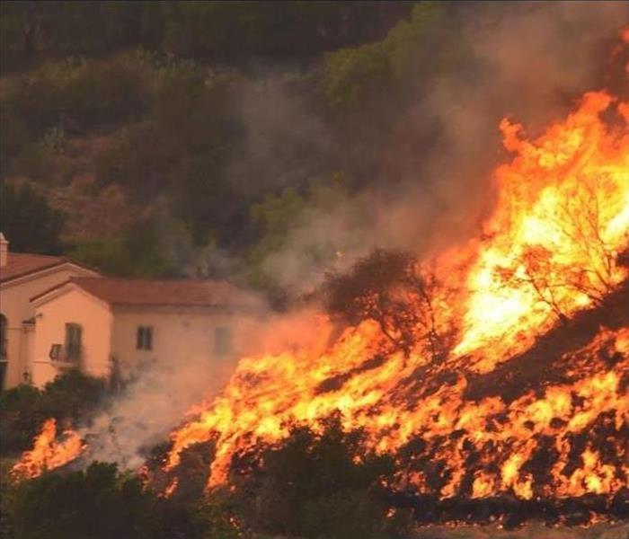 Fire burning through brush in front of houses.