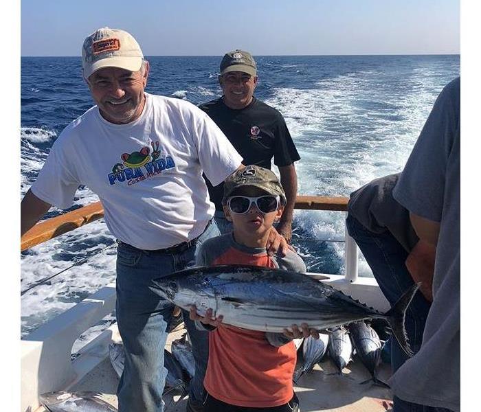 A boy holding a large fish on a boat in the ocean.